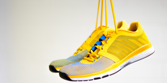 Gelbe Sportschuhe gehalten an den Schnürsenkeln 