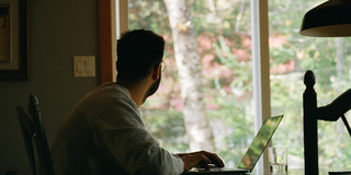 Mann sitzt vor dem Laptop und schaut aus dem Fenster