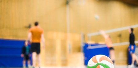 Volleyball in der Sporthalle mit Spielern und Netzt im Hintergrund 