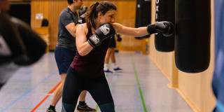Frau mit Boxhandschuhen boxt Boxsack